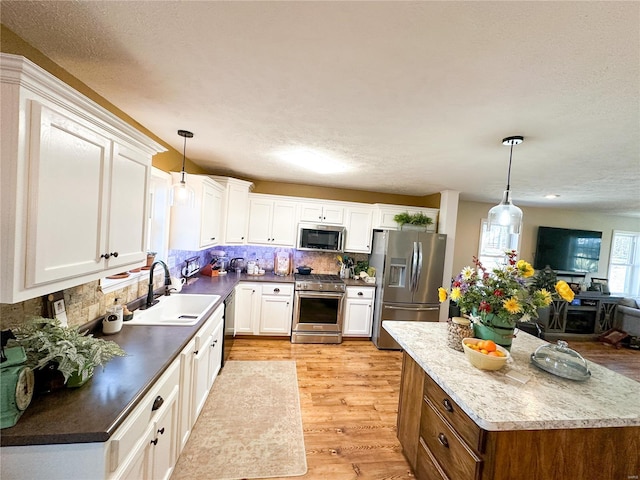 kitchen featuring sink, light hardwood / wood-style flooring, stainless steel appliances, white cabinets, and decorative light fixtures