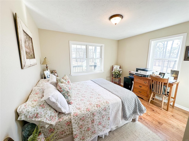 bedroom with multiple windows, light hardwood / wood-style floors, and a textured ceiling