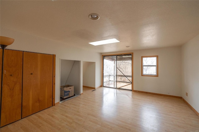 unfurnished bedroom with access to exterior, a skylight, light hardwood / wood-style floors, and a textured ceiling