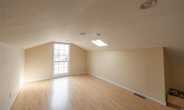 bonus room featuring lofted ceiling with skylight, a textured ceiling, and light wood-type flooring