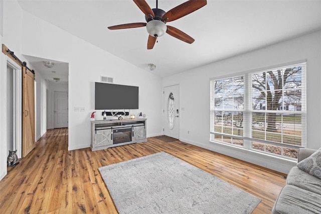 living room featuring ceiling fan, lofted ceiling, a barn door, and hardwood / wood-style floors