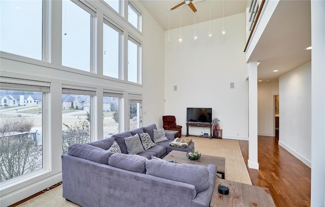 living room with a towering ceiling, a wealth of natural light, dark hardwood / wood-style floors, and ceiling fan