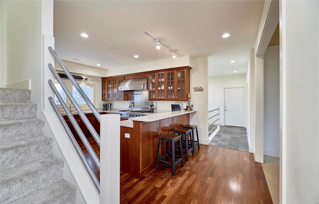 kitchen featuring dark hardwood / wood-style floors, a breakfast bar, range, kitchen peninsula, and wall chimney exhaust hood