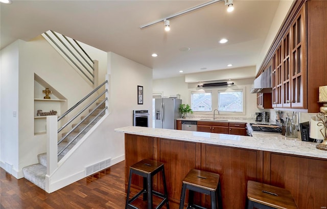 kitchen with dark wood-type flooring, a breakfast bar area, stainless steel appliances, light stone countertops, and kitchen peninsula