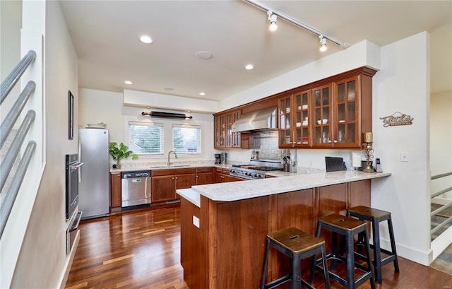 kitchen with wall chimney range hood, sink, stainless steel appliances, a kitchen bar, and kitchen peninsula