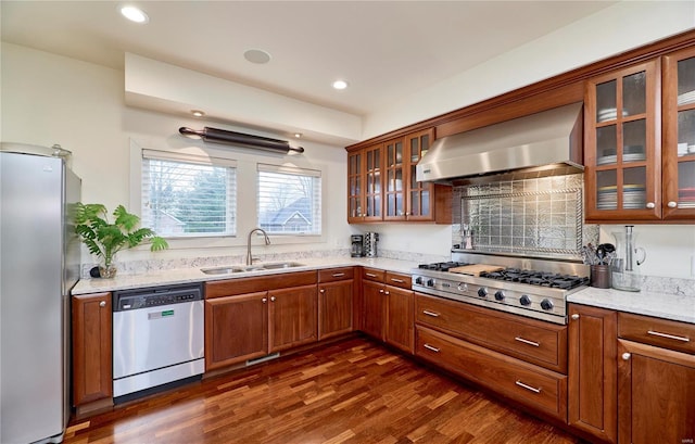 kitchen with wall chimney exhaust hood, sink, dark hardwood / wood-style flooring, stainless steel appliances, and light stone countertops