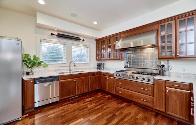 kitchen with sink, dark hardwood / wood-style flooring, stainless steel appliances, light stone countertops, and wall chimney exhaust hood