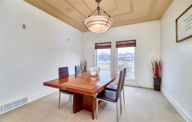 dining room featuring light colored carpet and a raised ceiling