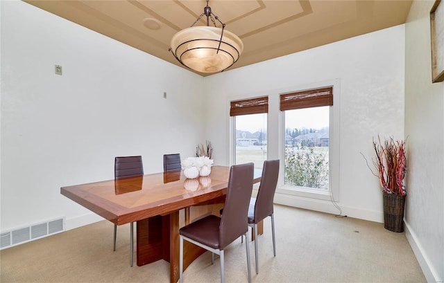 dining space with light carpet and a tray ceiling