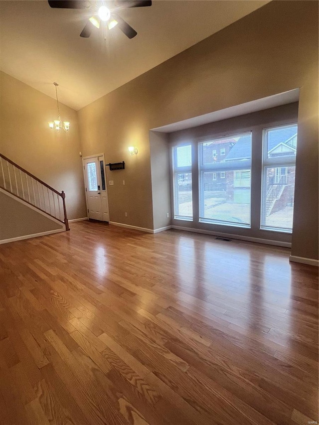 unfurnished living room featuring visible vents, stairway, wood finished floors, baseboards, and ceiling fan with notable chandelier