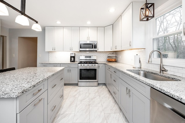 kitchen with appliances with stainless steel finishes, sink, light stone counters, and decorative light fixtures