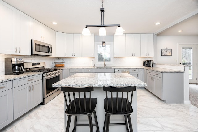 kitchen featuring a kitchen island, appliances with stainless steel finishes, decorative light fixtures, gray cabinetry, and light stone counters