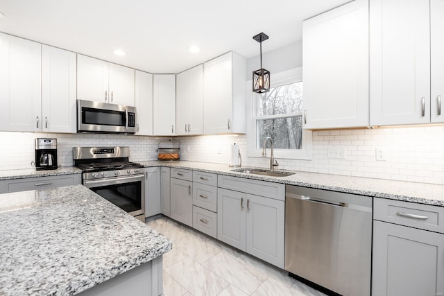 kitchen with pendant lighting, sink, light stone counters, and stainless steel appliances