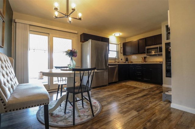 kitchen featuring dark wood-type flooring, a chandelier, pendant lighting, stainless steel appliances, and decorative backsplash