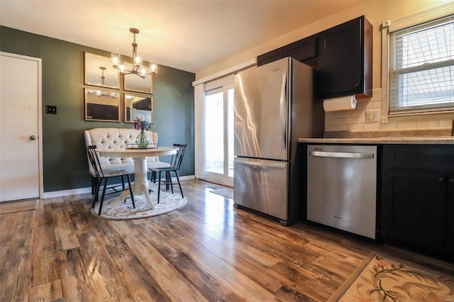 kitchen featuring hardwood / wood-style flooring, appliances with stainless steel finishes, a notable chandelier, decorative backsplash, and decorative light fixtures