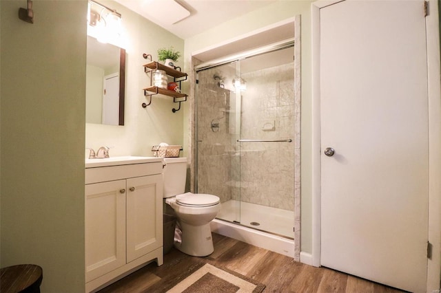 bathroom with wood-type flooring, toilet, a shower with door, and vanity