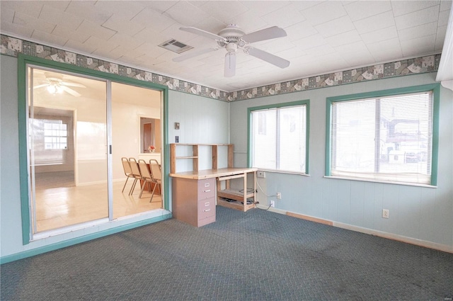 unfurnished office featuring ceiling fan, a healthy amount of sunlight, and dark colored carpet