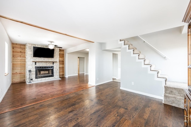 unfurnished living room with dark hardwood / wood-style flooring, a stone fireplace, wooden walls, and ceiling fan