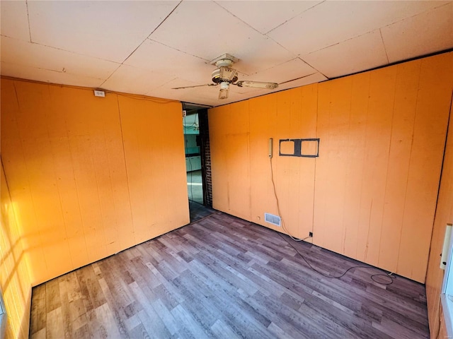 spare room with hardwood / wood-style floors, wooden walls, and ceiling fan