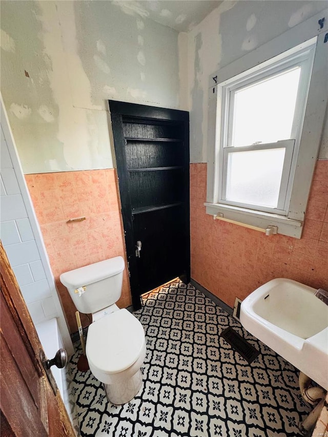 bathroom featuring tile patterned floors, toilet, and tile walls