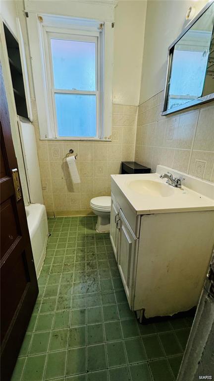 bathroom with vanity, a washtub, tile walls, and toilet