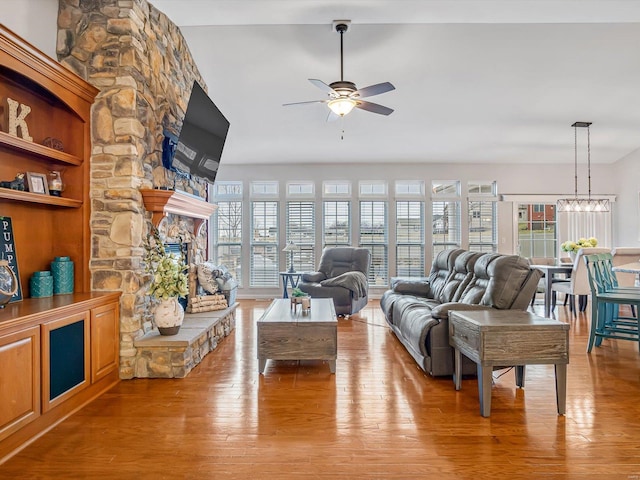 living room featuring a stone fireplace, ceiling fan with notable chandelier, and light wood-type flooring