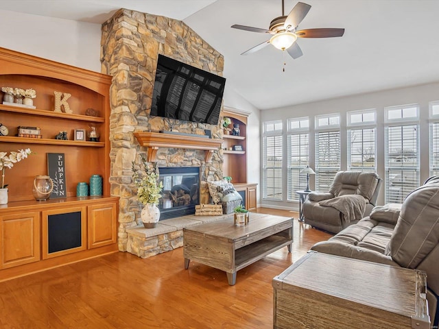 living room with ceiling fan, a fireplace, vaulted ceiling, and light wood-type flooring