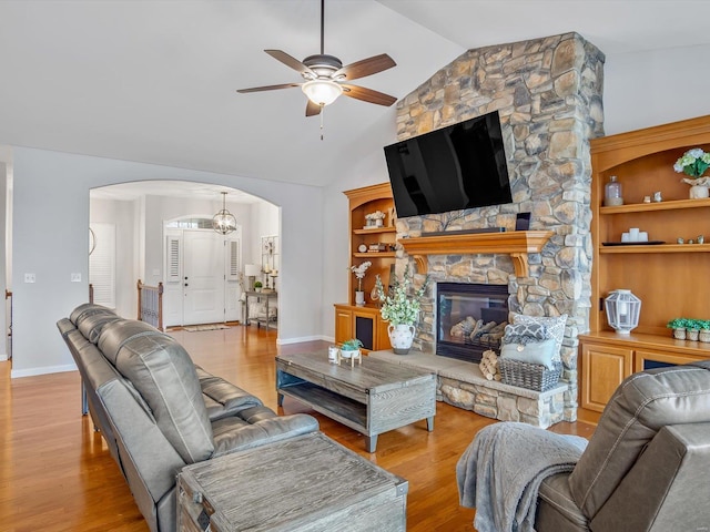 living room featuring ceiling fan, a fireplace, vaulted ceiling, and light wood-type flooring