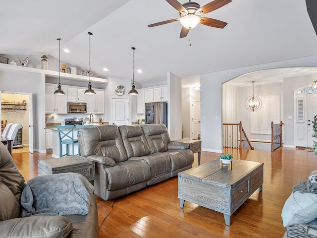 living room with lofted ceiling, ceiling fan with notable chandelier, and light hardwood / wood-style flooring