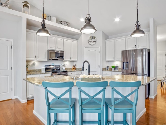 kitchen featuring white cabinetry, stainless steel appliances, light stone counters, and a center island with sink