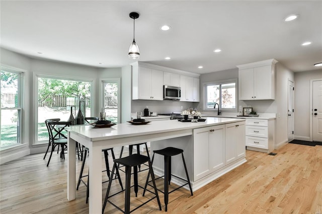 kitchen featuring hanging light fixtures, sink, white cabinets, and light wood-type flooring