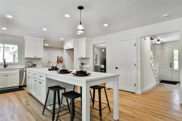 kitchen featuring a breakfast bar, light hardwood / wood-style flooring, hanging light fixtures, stainless steel dishwasher, and white cabinets