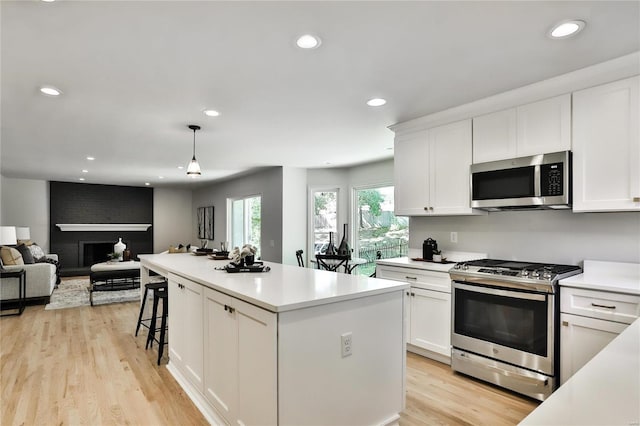 kitchen featuring appliances with stainless steel finishes, pendant lighting, white cabinetry, a center island, and a brick fireplace