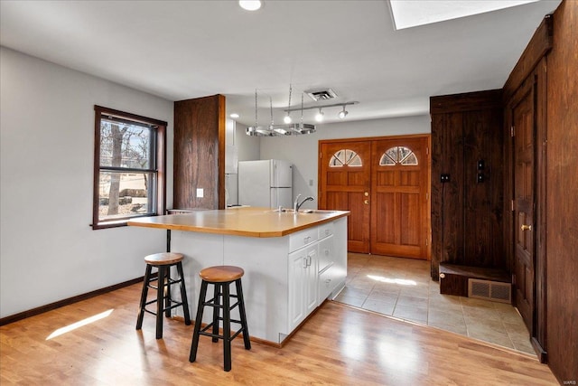 kitchen with visible vents, light wood-type flooring, freestanding refrigerator, white cabinets, and a sink