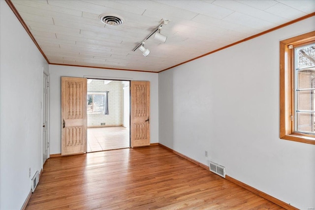 empty room with light wood finished floors, visible vents, and crown molding