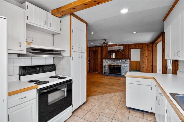 kitchen featuring range with electric cooktop, a ceiling fan, a stone fireplace, light countertops, and light tile patterned floors