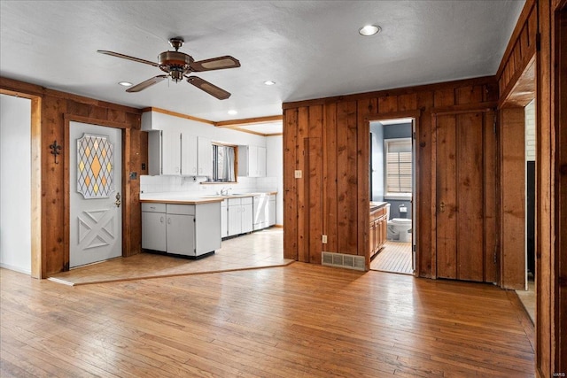 kitchen with light wood finished floors, ceiling fan, light countertops, wood walls, and dishwasher