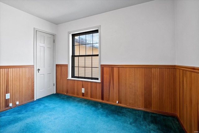 empty room featuring carpet floors, wood walls, and wainscoting