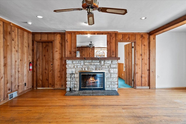 unfurnished living room featuring wooden walls, wood finished floors, visible vents, and ceiling fan