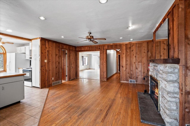 unfurnished living room featuring visible vents, a stone fireplace, ceiling fan, and light wood finished floors