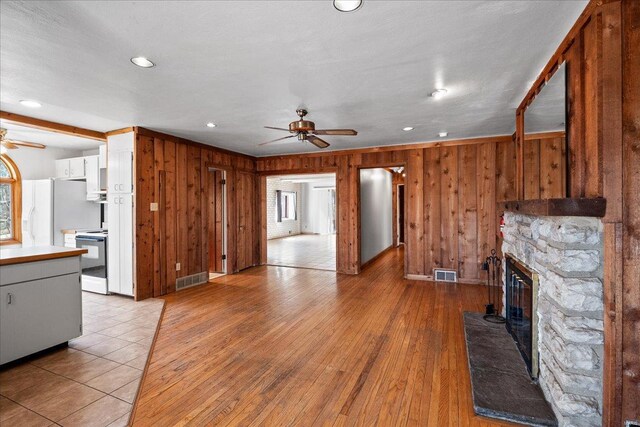 unfurnished living room featuring visible vents, a stone fireplace, ceiling fan, and light wood-style flooring