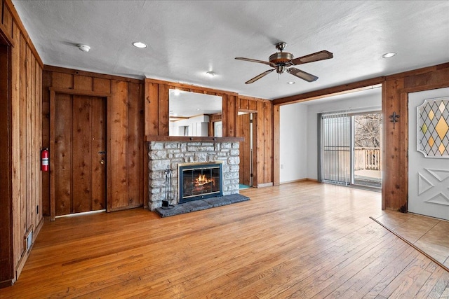 unfurnished living room featuring light wood finished floors, a fireplace, ceiling fan, wood walls, and a textured ceiling