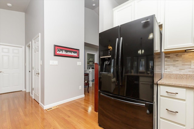 kitchen featuring black fridge, backsplash, light wood-type flooring, and white cabinets