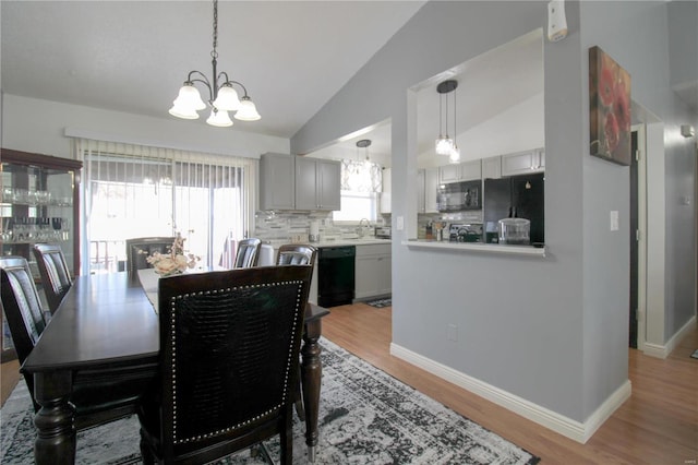 dining area featuring light hardwood / wood-style flooring, a notable chandelier, vaulted ceiling, and sink