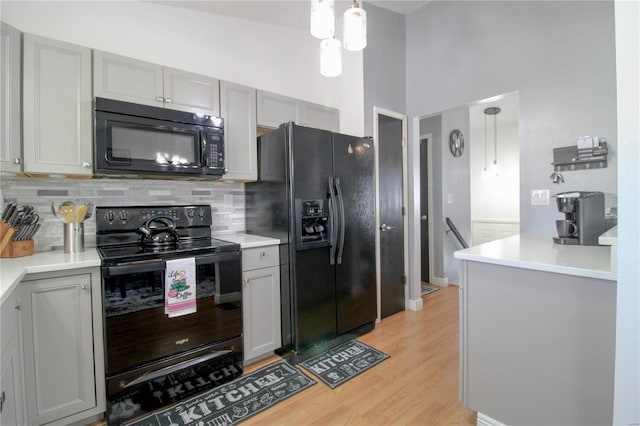 kitchen with light hardwood / wood-style flooring, gray cabinets, hanging light fixtures, backsplash, and black appliances