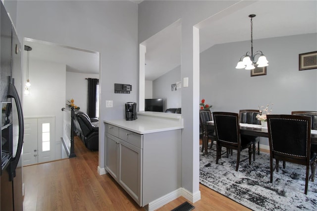 kitchen with black fridge, decorative light fixtures, vaulted ceiling, gray cabinets, and light hardwood / wood-style floors