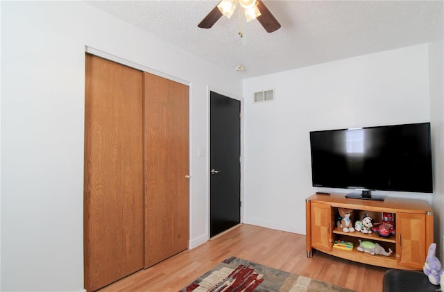 living room featuring ceiling fan, a textured ceiling, and light hardwood / wood-style floors