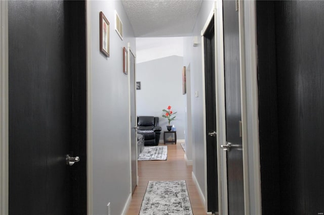 corridor with a textured ceiling and light hardwood / wood-style flooring