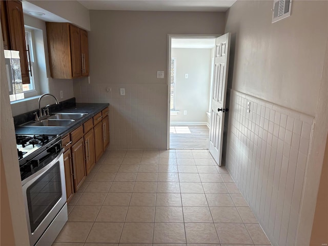 kitchen with tile walls, sink, stainless steel gas range oven, and light tile patterned flooring