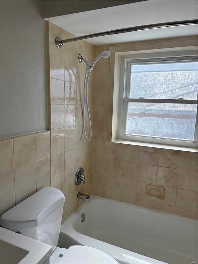 bathroom featuring tiled shower / bath, tile walls, and toilet